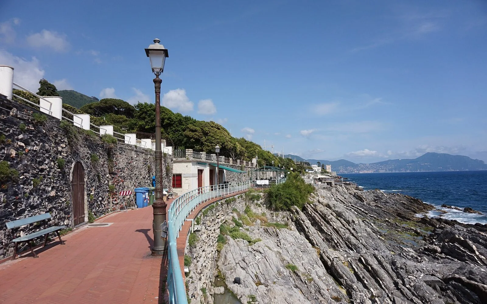 La passeggiata Anita Garibaldi a Nervi con il lastricato rosso, i lampioni e la ringhiera azzurra sopra gli scogli, con il mare blu e la costa sullo sfondo
