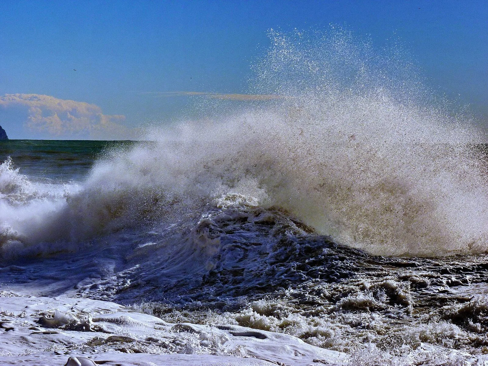 Onda che si infrange in una mareggiata invernale sul mare di Genova sotto un cielo azzurro